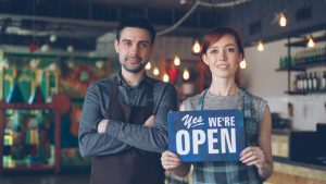 A happy couple welcomes customers: we are open.