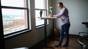 man in purple dress shirt and blue denim jeans standing beside window